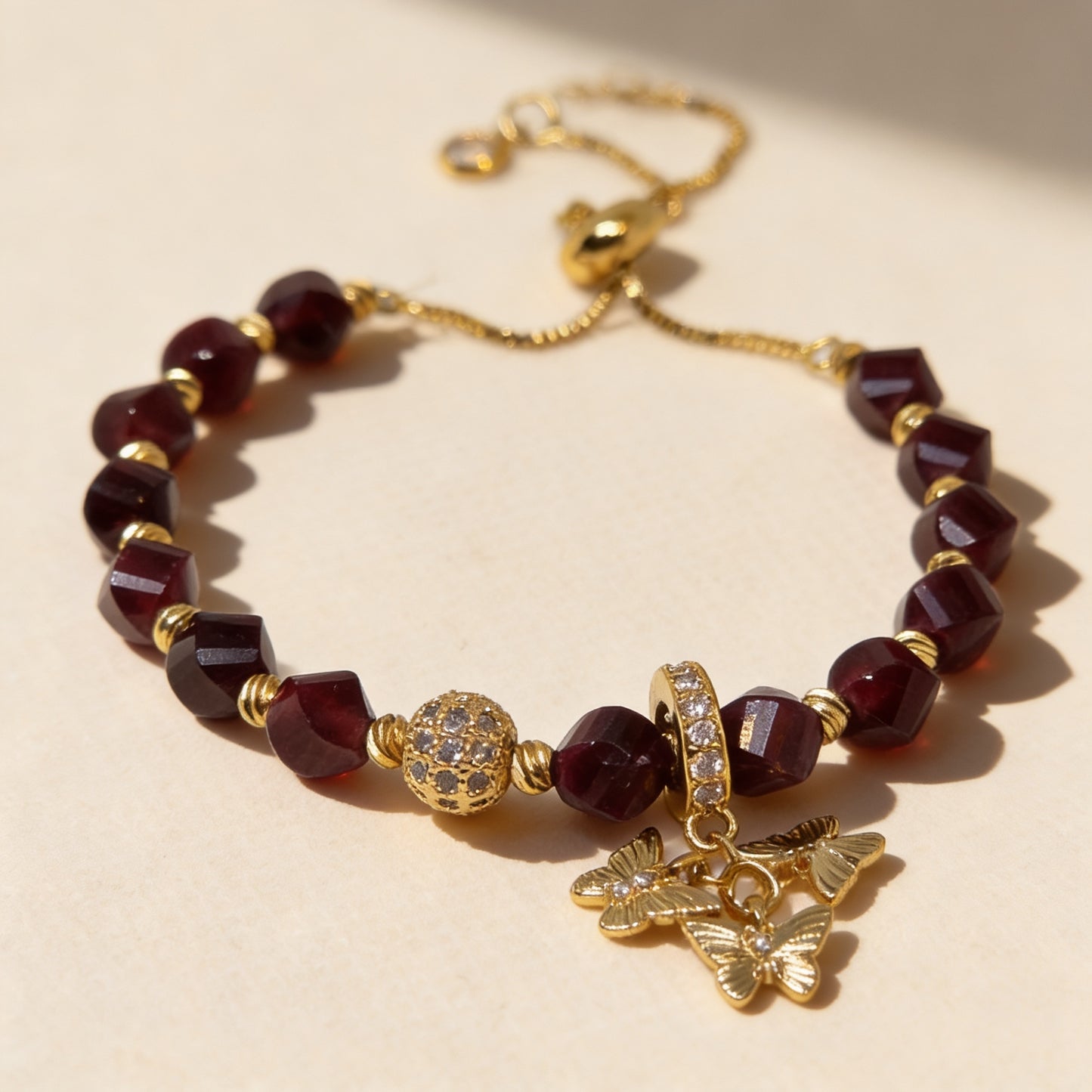 Handmade garnet gemstone bracelet with gold-plated accents, zircon pavé bead and butterfly charms on a neutral background.
